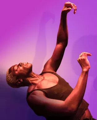 A dancer is performing in front of a purple background.