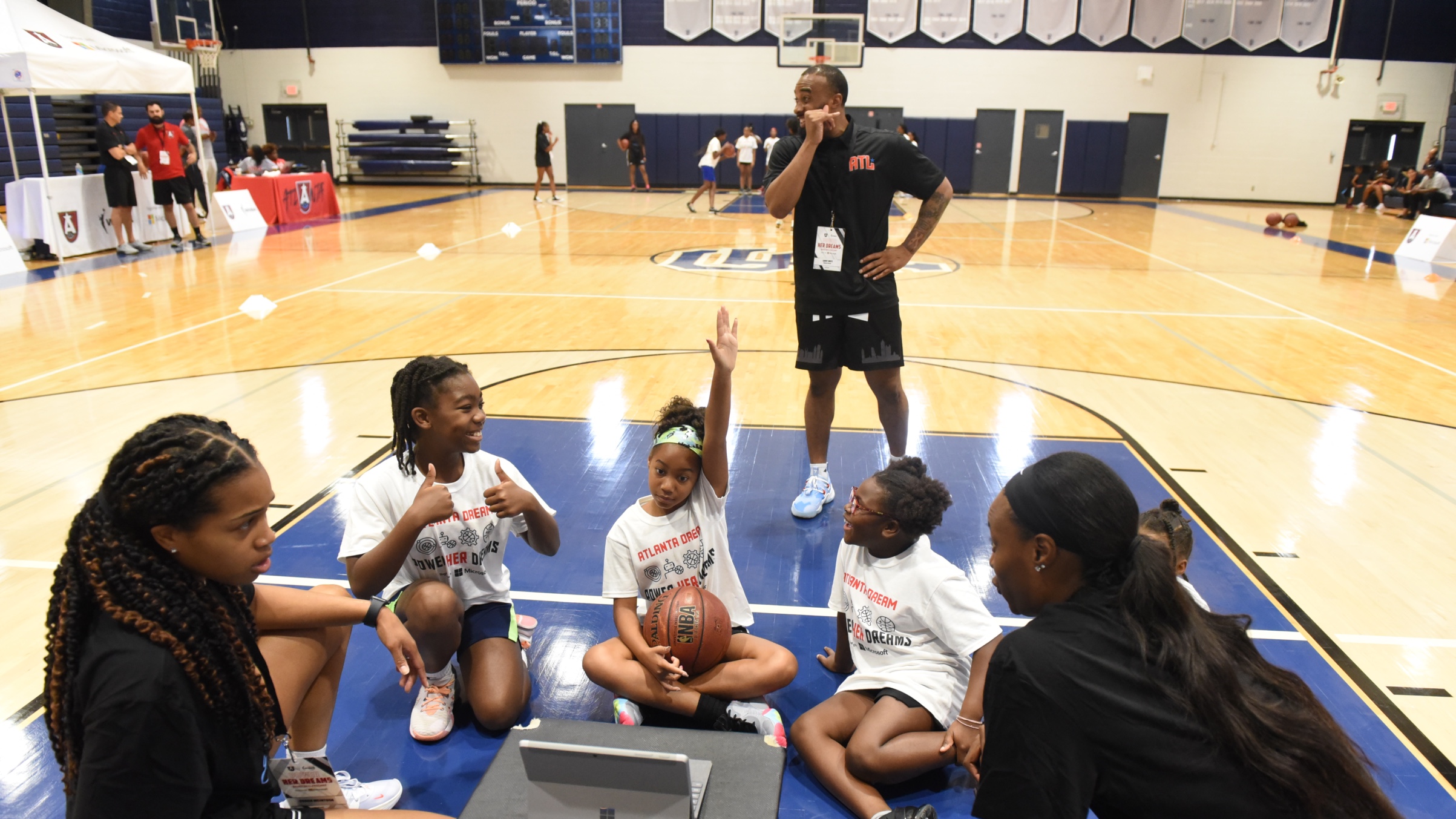 A coach addressing young basketball players during a training session in an indoor court.