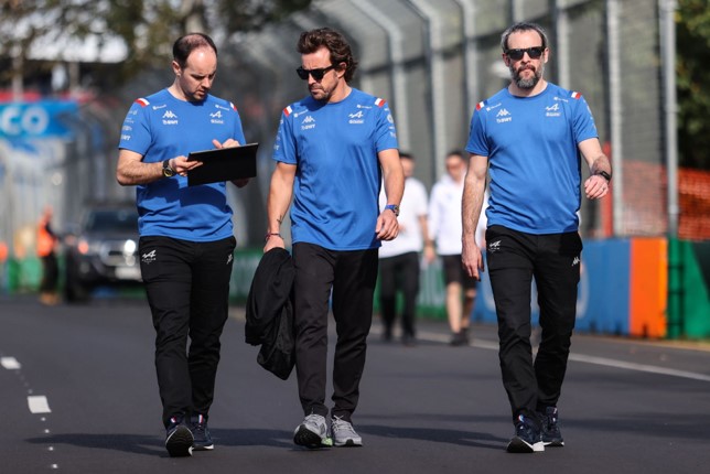 Fernando Alonso walks belong two BWT Alpine F1 Team engineers on the F1 track while they look at data on a Microsoft Surface tablet.