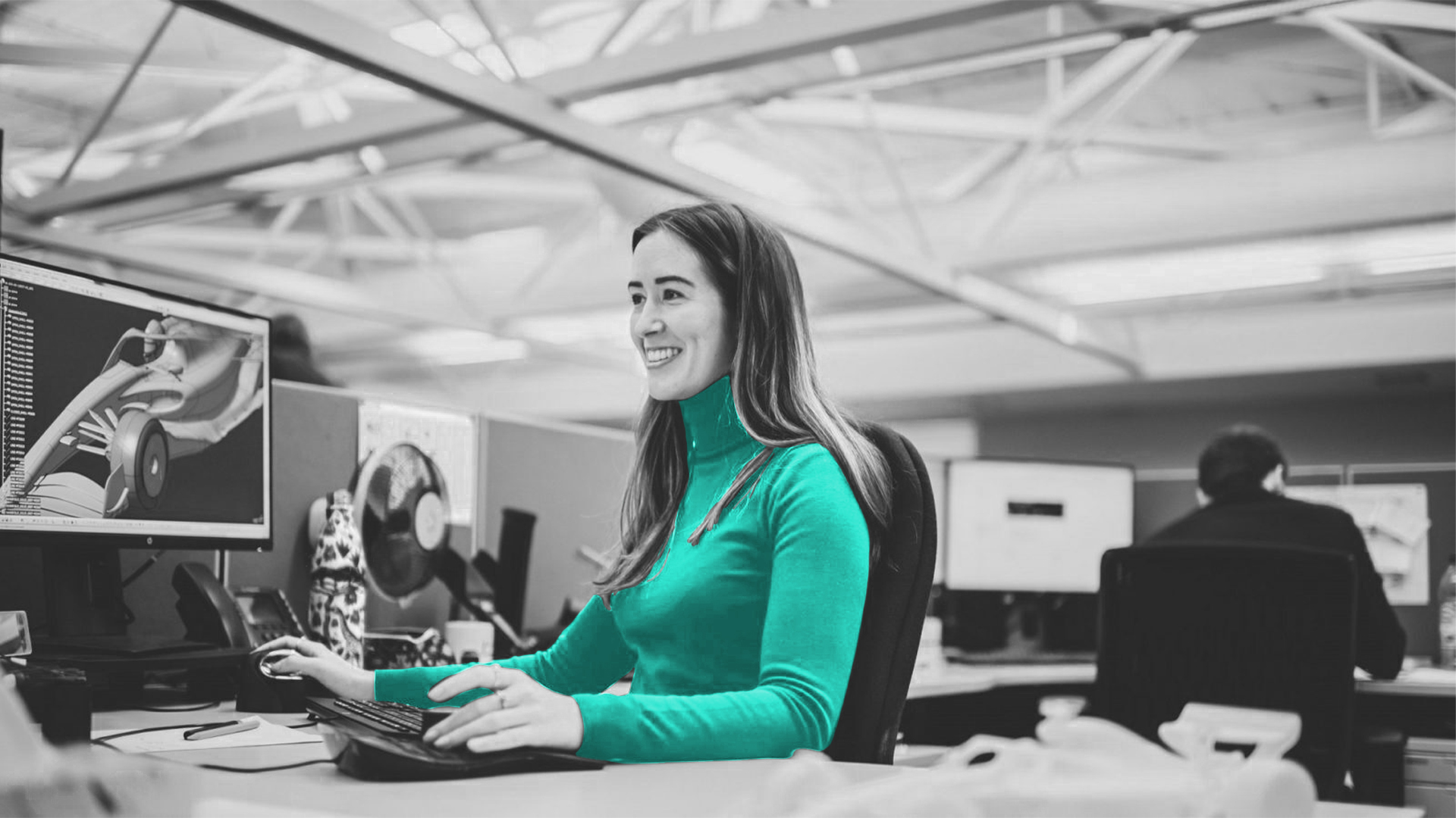 Black and white portrait of BWT Alpine F1’s Elizabeth Apthrop sitting at a desk working on a computer. She is wearing a neon blue turtleneck shirt.