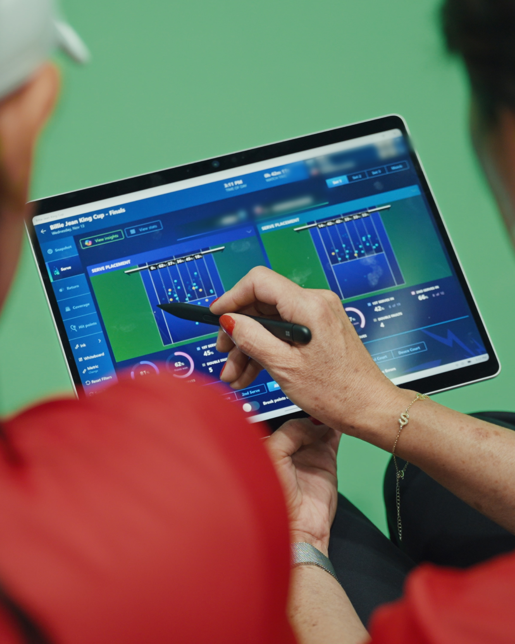 Two people examine tennis match analytics on a tablet, one pointing with a pen at the screen.