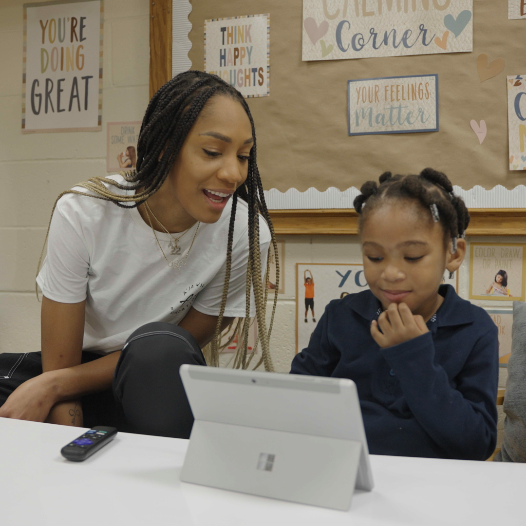 A’ja Wilson sits next to a young girl and smiles as they look at a Surface device.