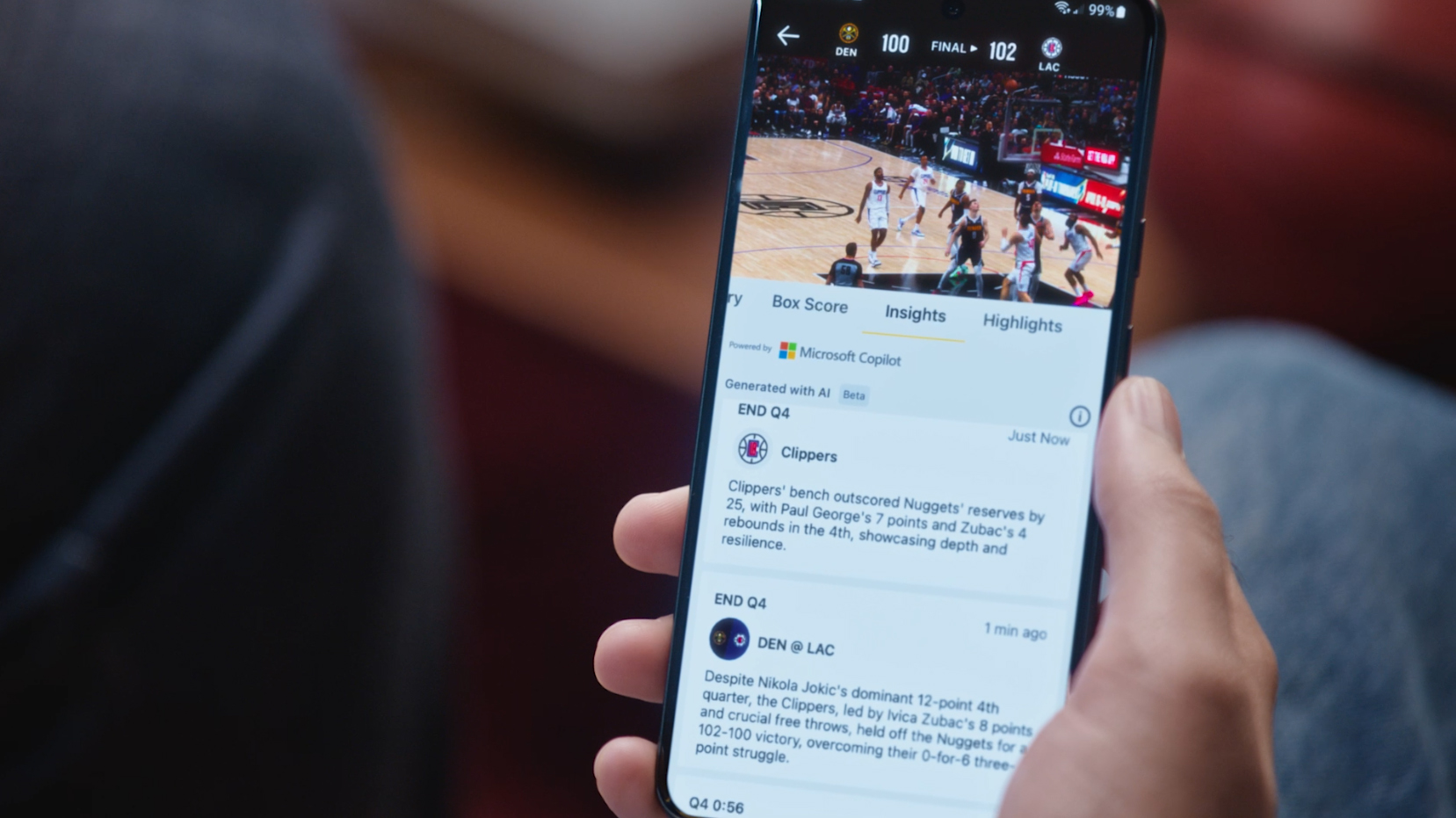 A person holding a smartphone displaying a basketball game score and related stats on a sports app.