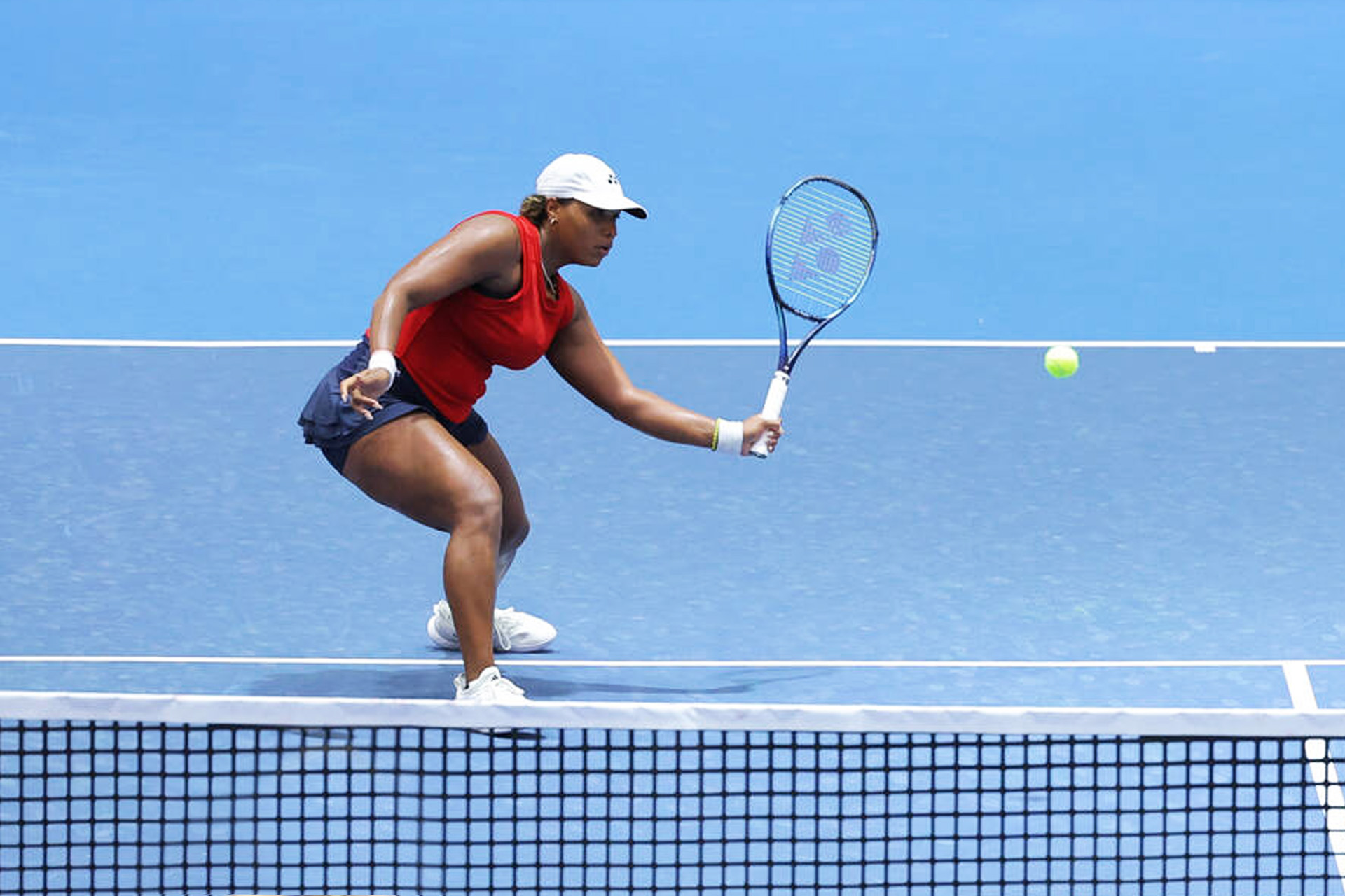 Female tennis player preparing for a backhand return on a blue court.