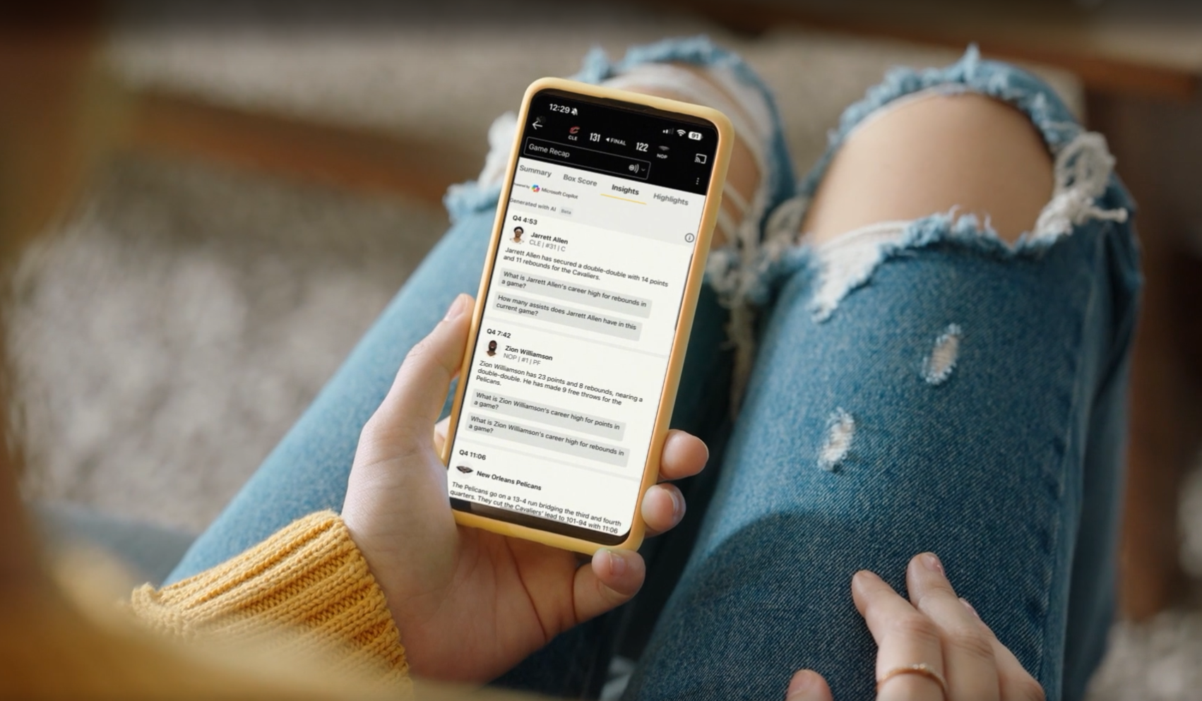 Person holding a yellow smartphone showing a messaging app, while wearing ripped jeans and a yellow sweater.