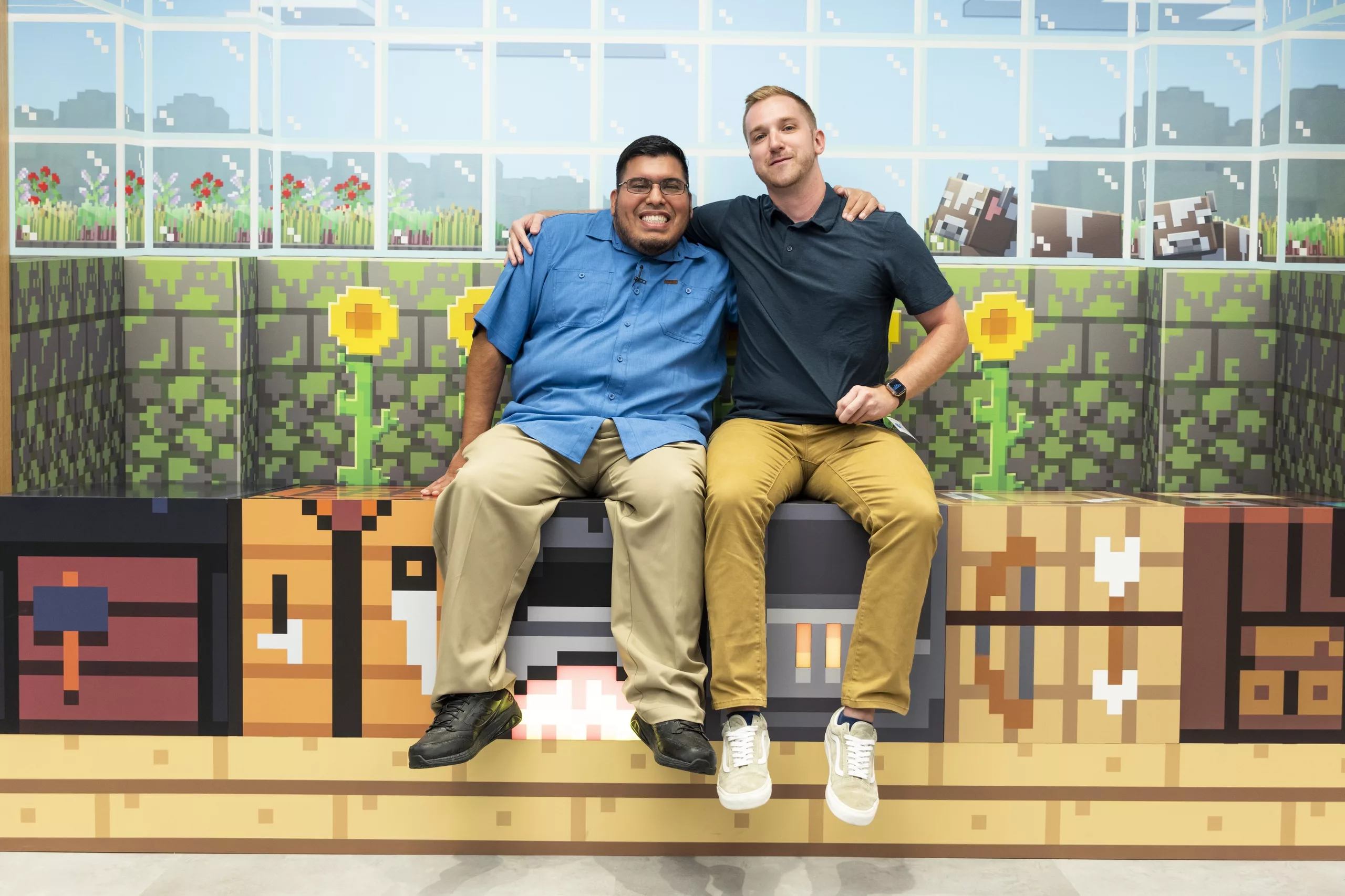 Two men sit smiling in a production set with walls made to look like the Minecraft “building-block” aesthetic.