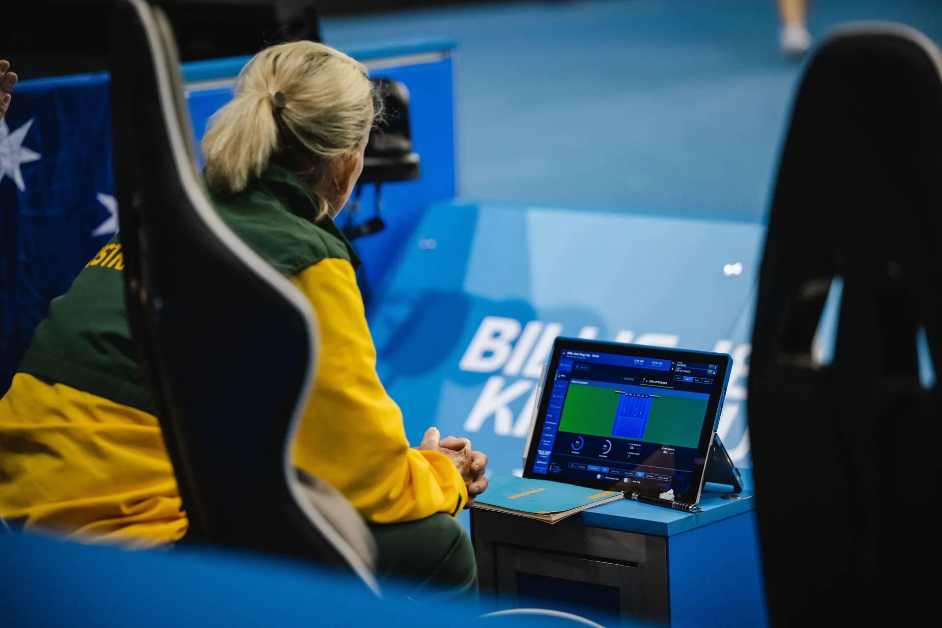 Woman seated looking at Surface device in front tennis court.