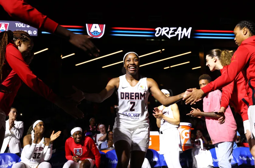 A Dream basketball player wearing a white uniform smiles as she high-fives other teammates.