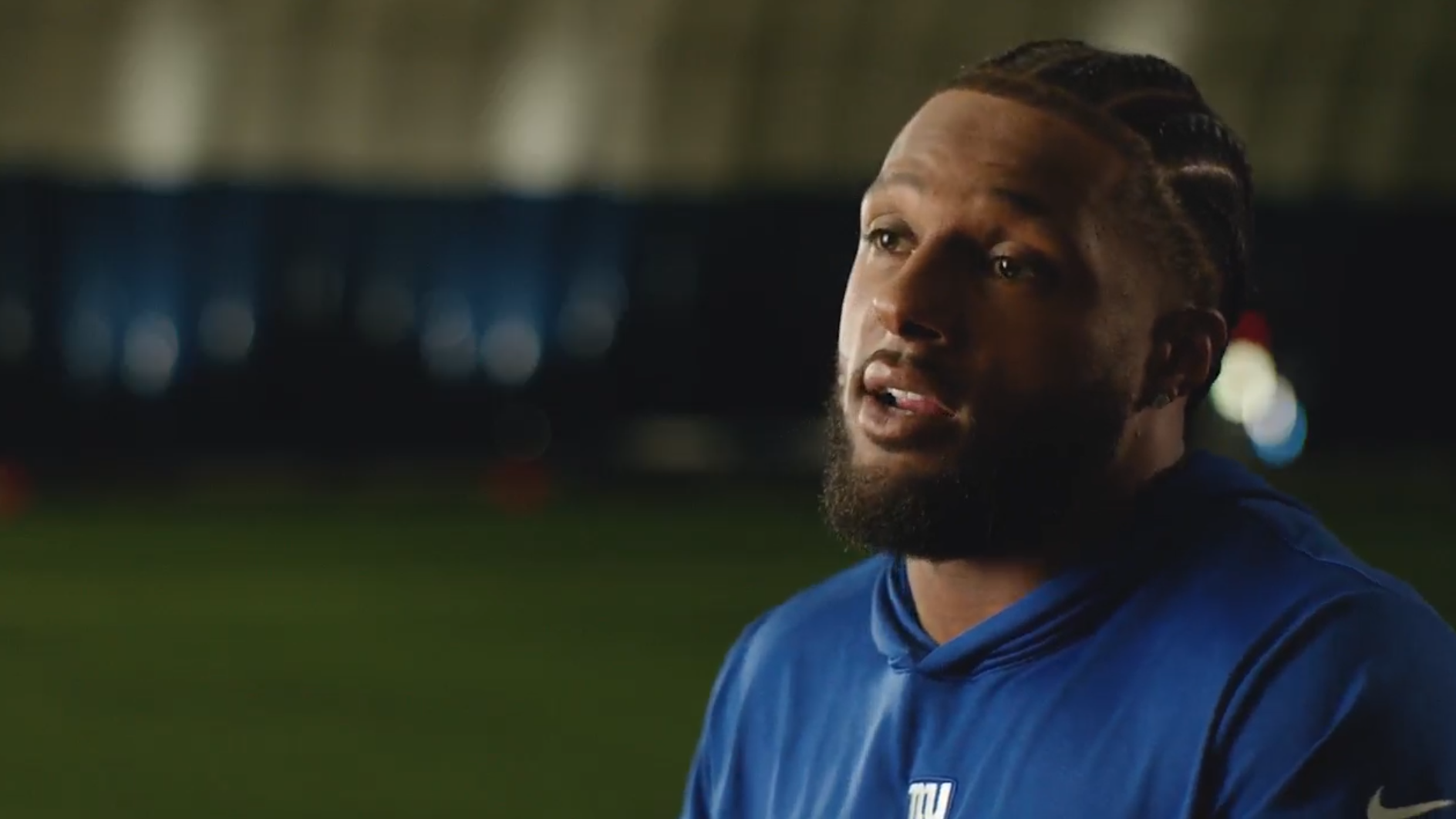 Person in a blue hoodie speaking in an indoor sports facility.