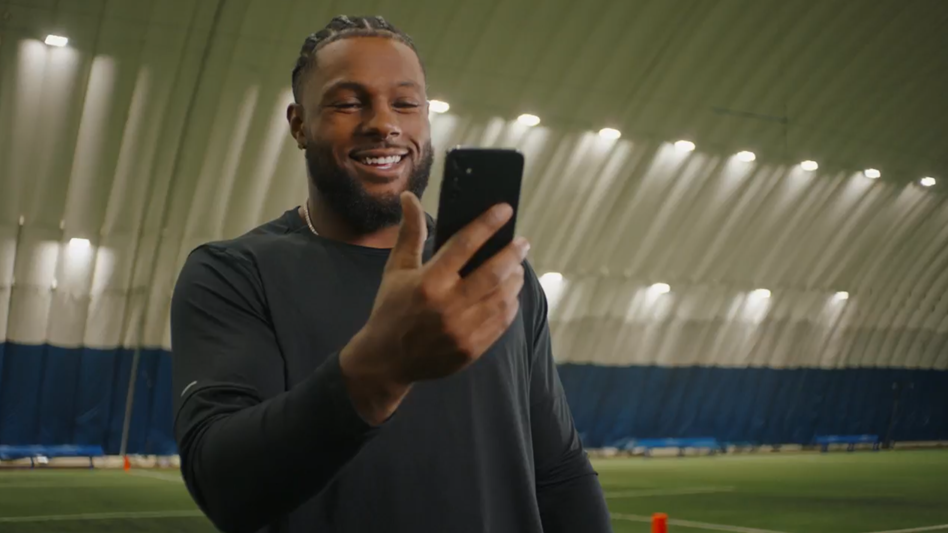 A man in a black shirt smiles at a smartphone inside a large, well-lit dome.