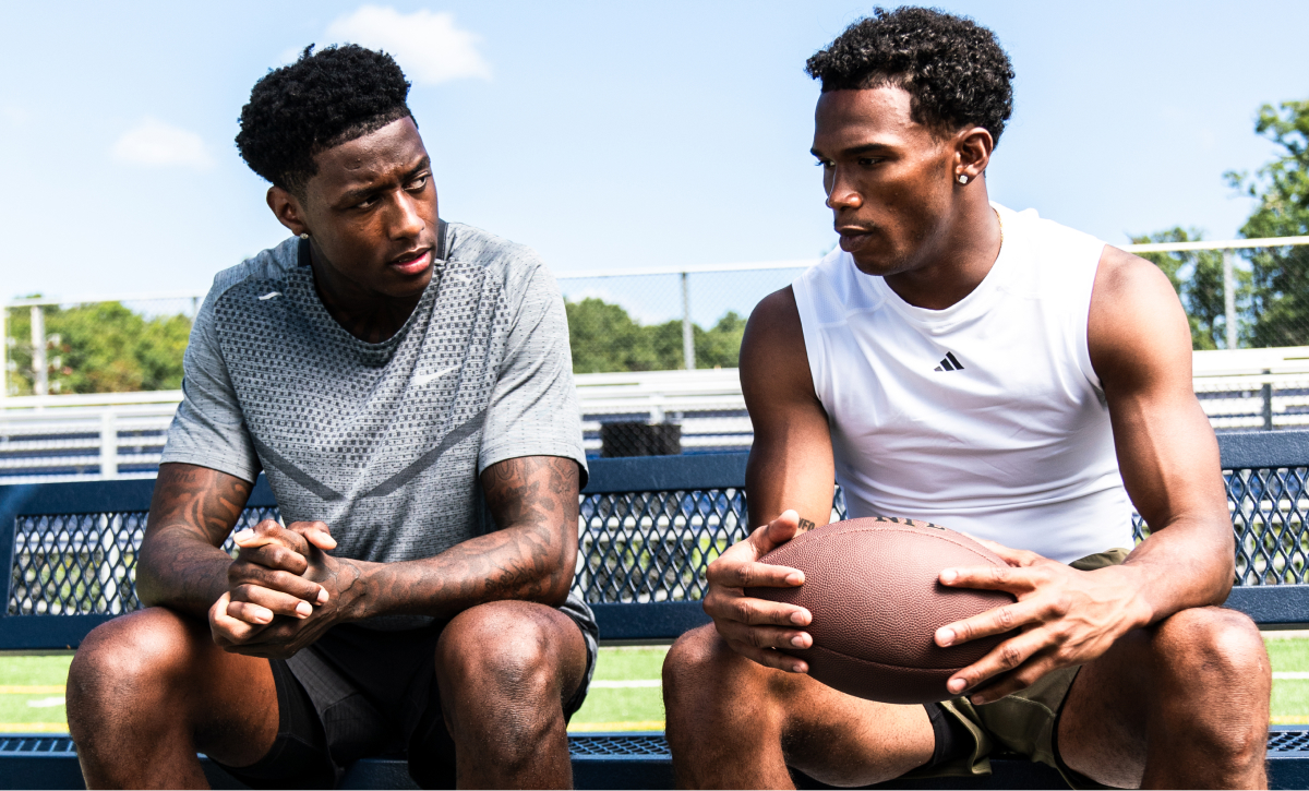 Two football players sitting on a bench with a ball.