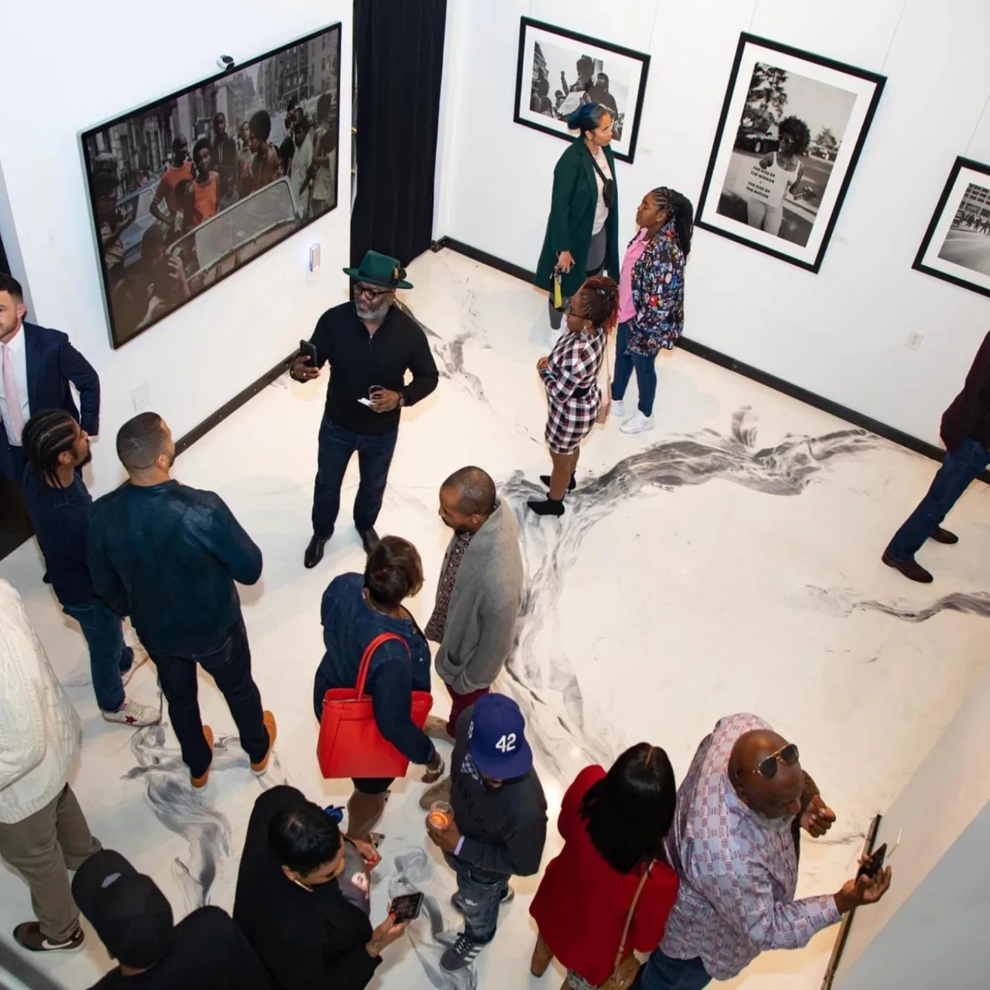 Bird’s-eye view of a group of people standing in an art gallery with framed art hanging on white walls