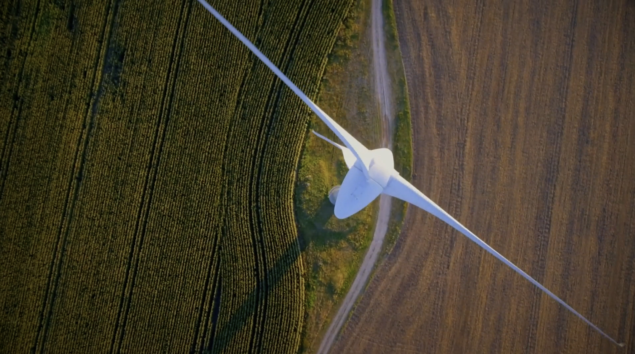 Arial view of a large wind turbine amid green fields on one side and brown fields on the other.