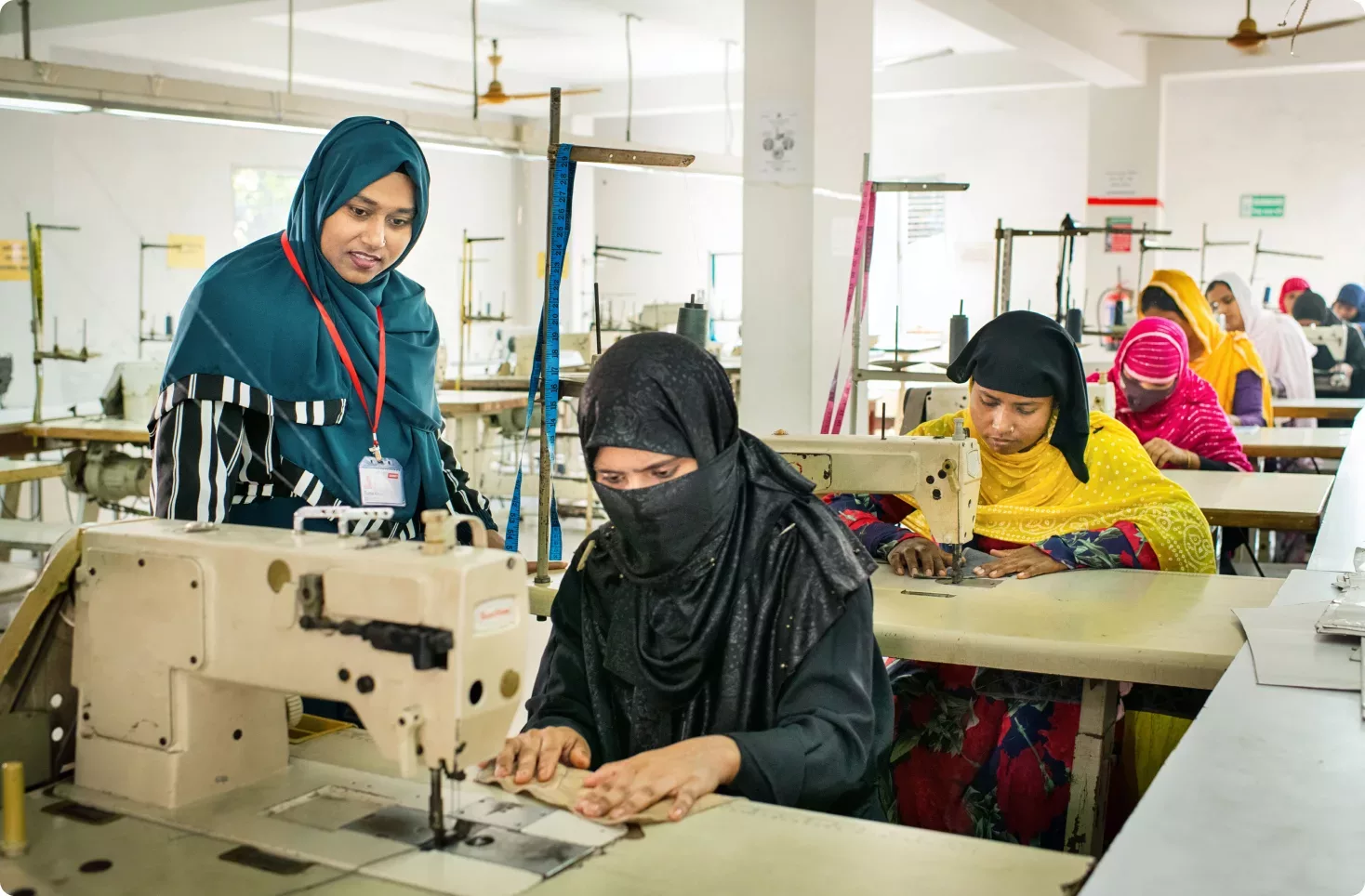 Ruma oversees a line of women in the garment factory while they sit and work on sewing machines.