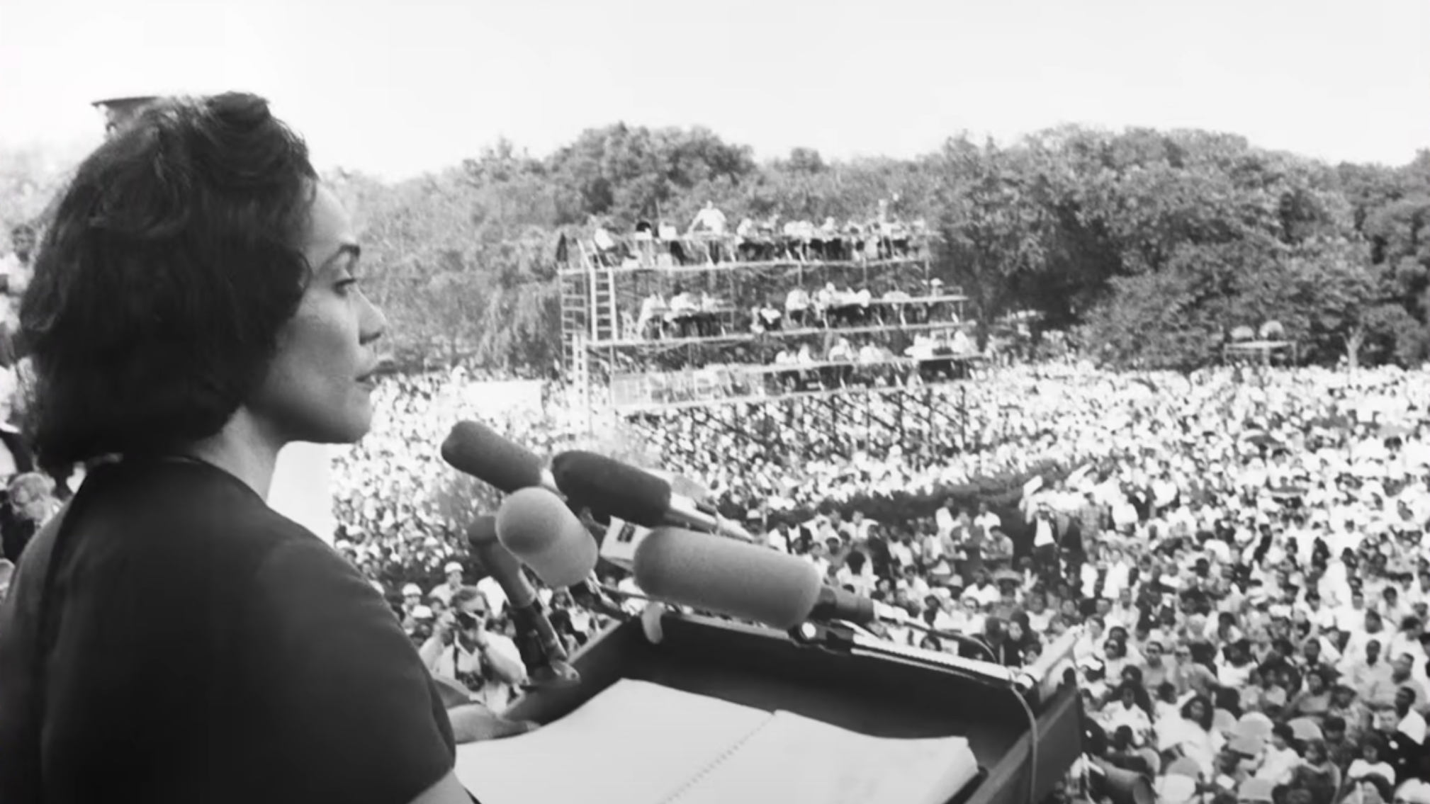 An old black and white photo of a woman standing in front of a crowd.