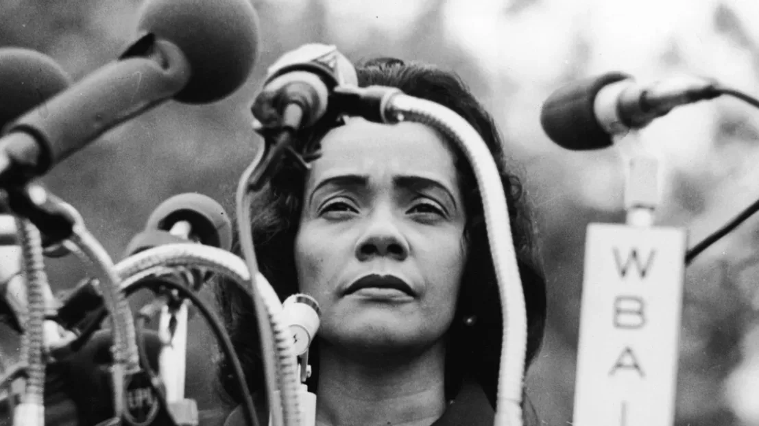 Black and white close-up photograph of Coretta Scott King looking off into the distance with several microphones in front of her
