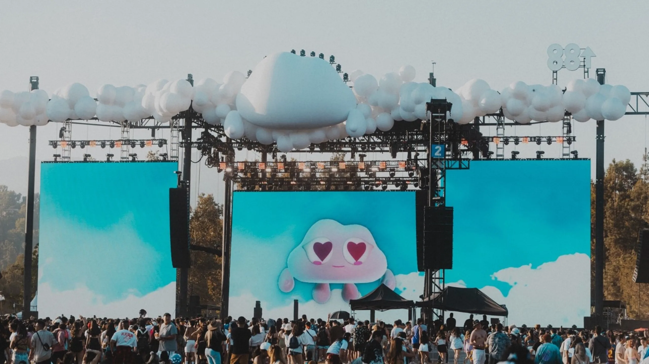 A crowd of people in front of a large stage with a screen displaying a cloud, with cloud decorations on the top