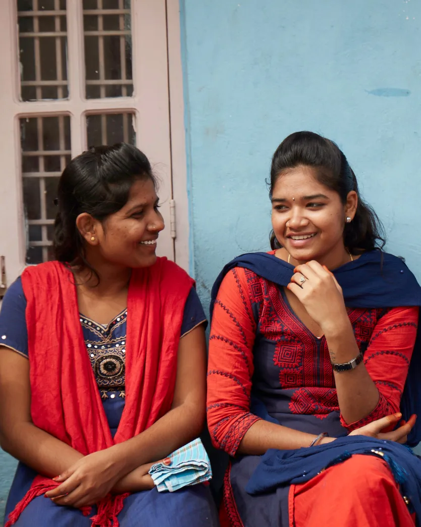 Two indian women sitting on a bench and smiling.