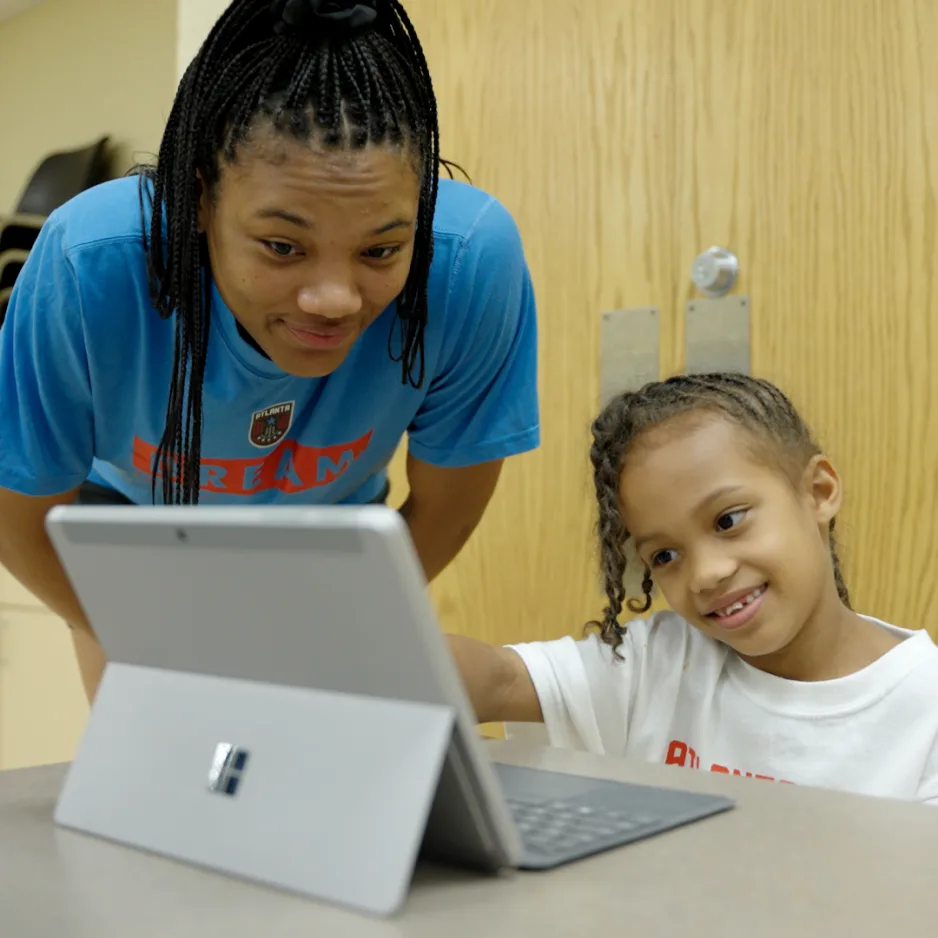 A woman and a young girl smile as they look at a Surface device.