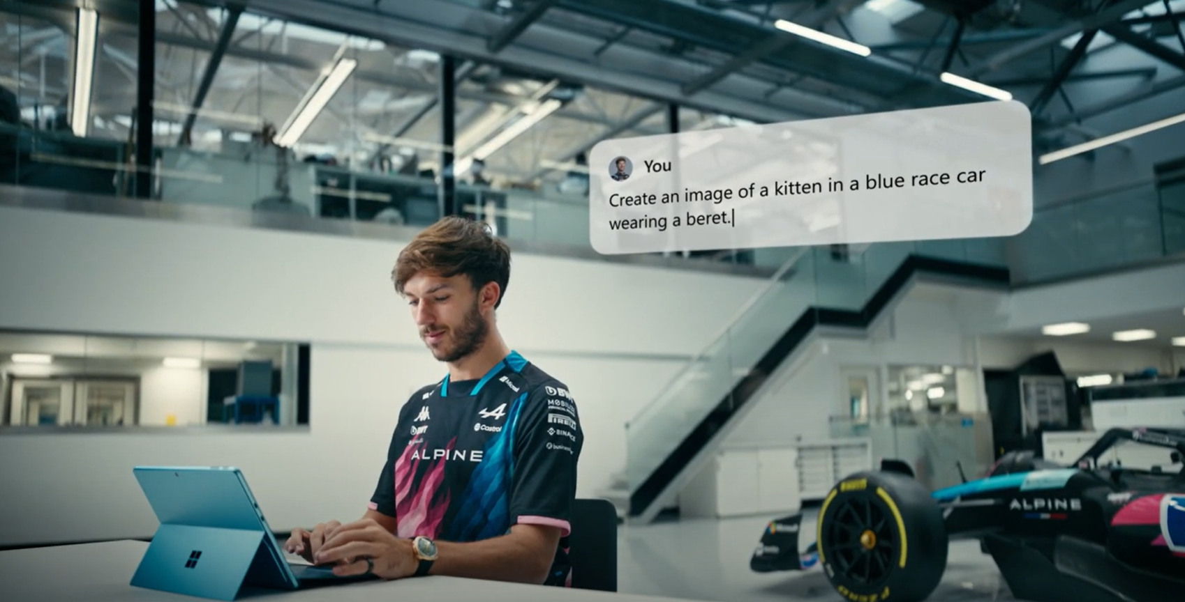 A person wearing an Alpine racing shirt is typing on a Microsoft Surface laptop in a modern office. A message on screen reads, "Create an image of a kitten in a blue race car wearing a beret.