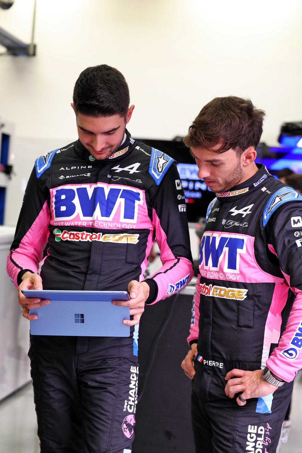 Two racing drivers looking at a tablet in a garage.