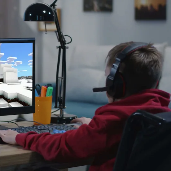A young child in a red sweatshirt plays video games on his computer. He is wearing a gaming headset.