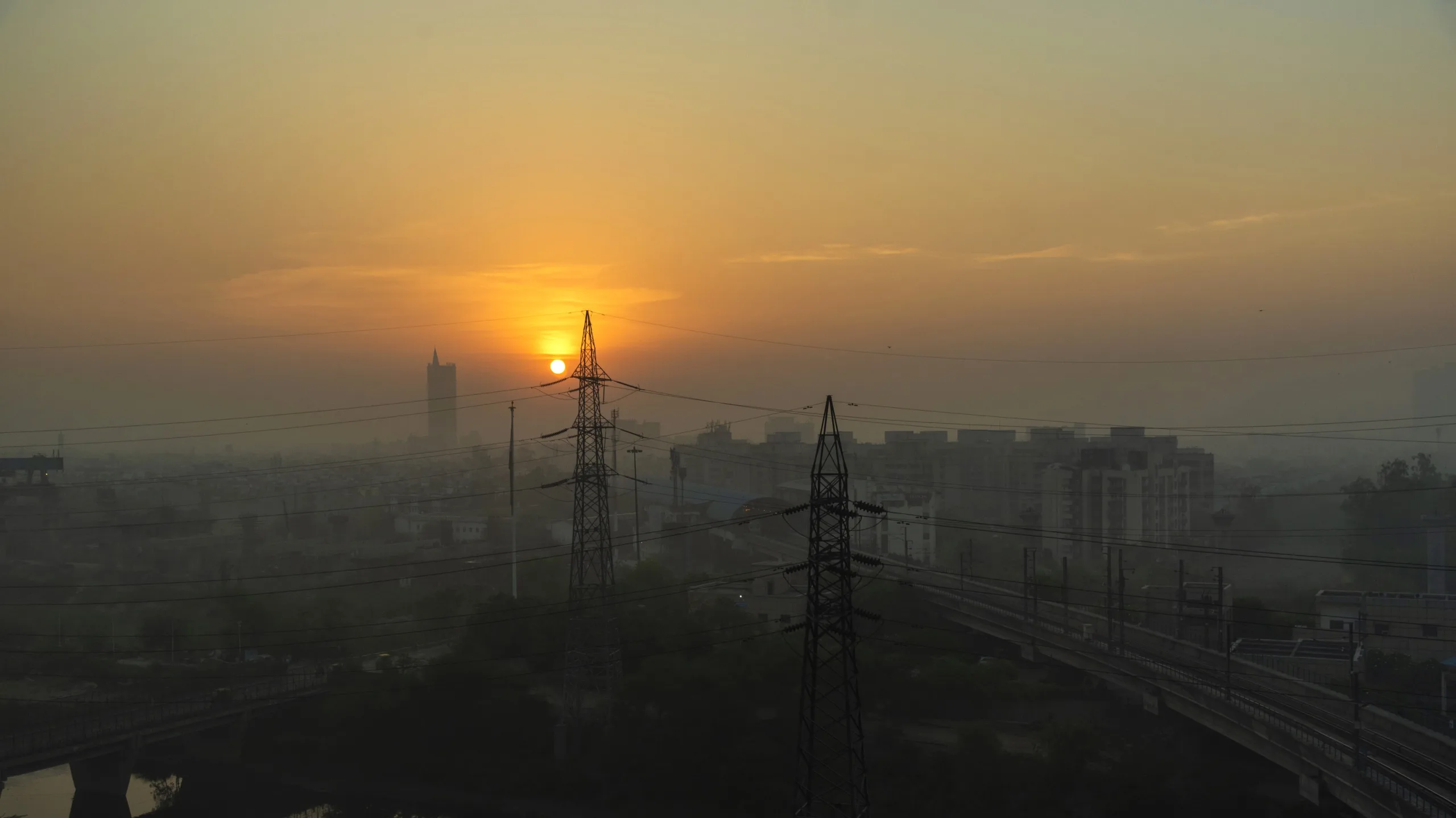 The sun rises over a city with power lines.