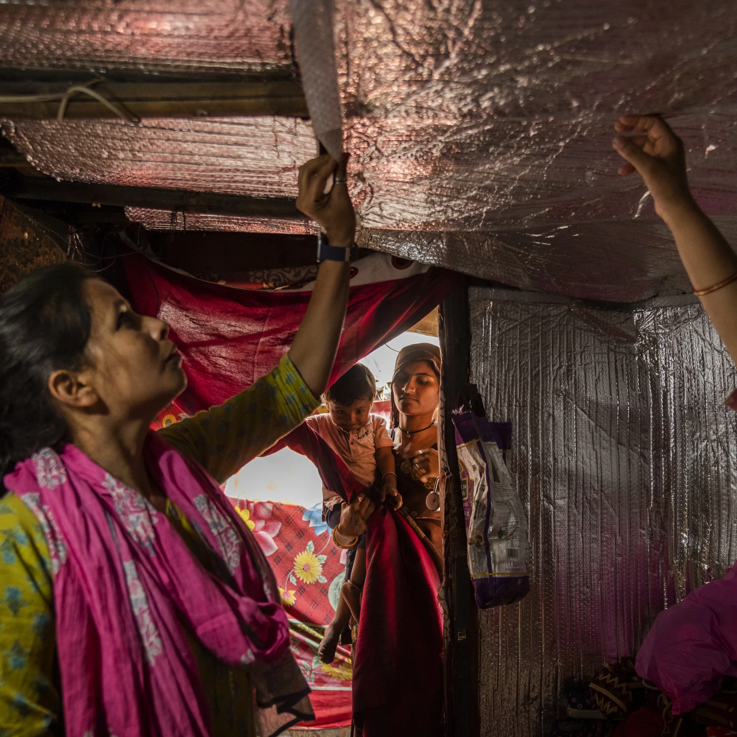 A woman looks at the insulation inside of a home while a mother and child look on from the doorway. 