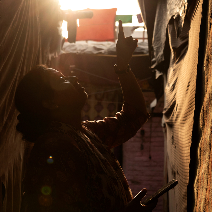 A woman stands outside of a home in a densely packed neighborhood and points to its roof.