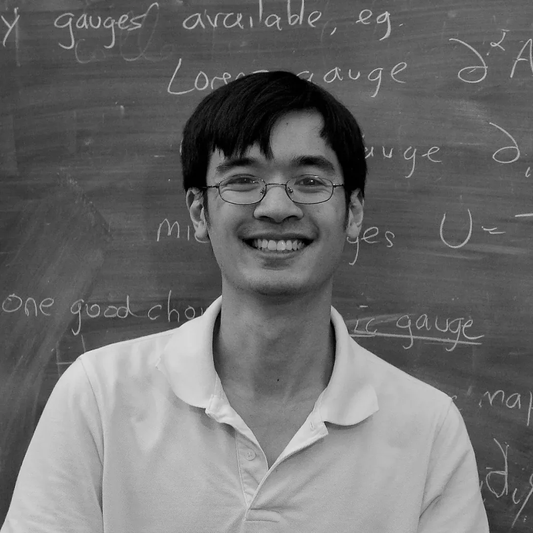 A black and white photo of a man smiling in front of a blackboard.