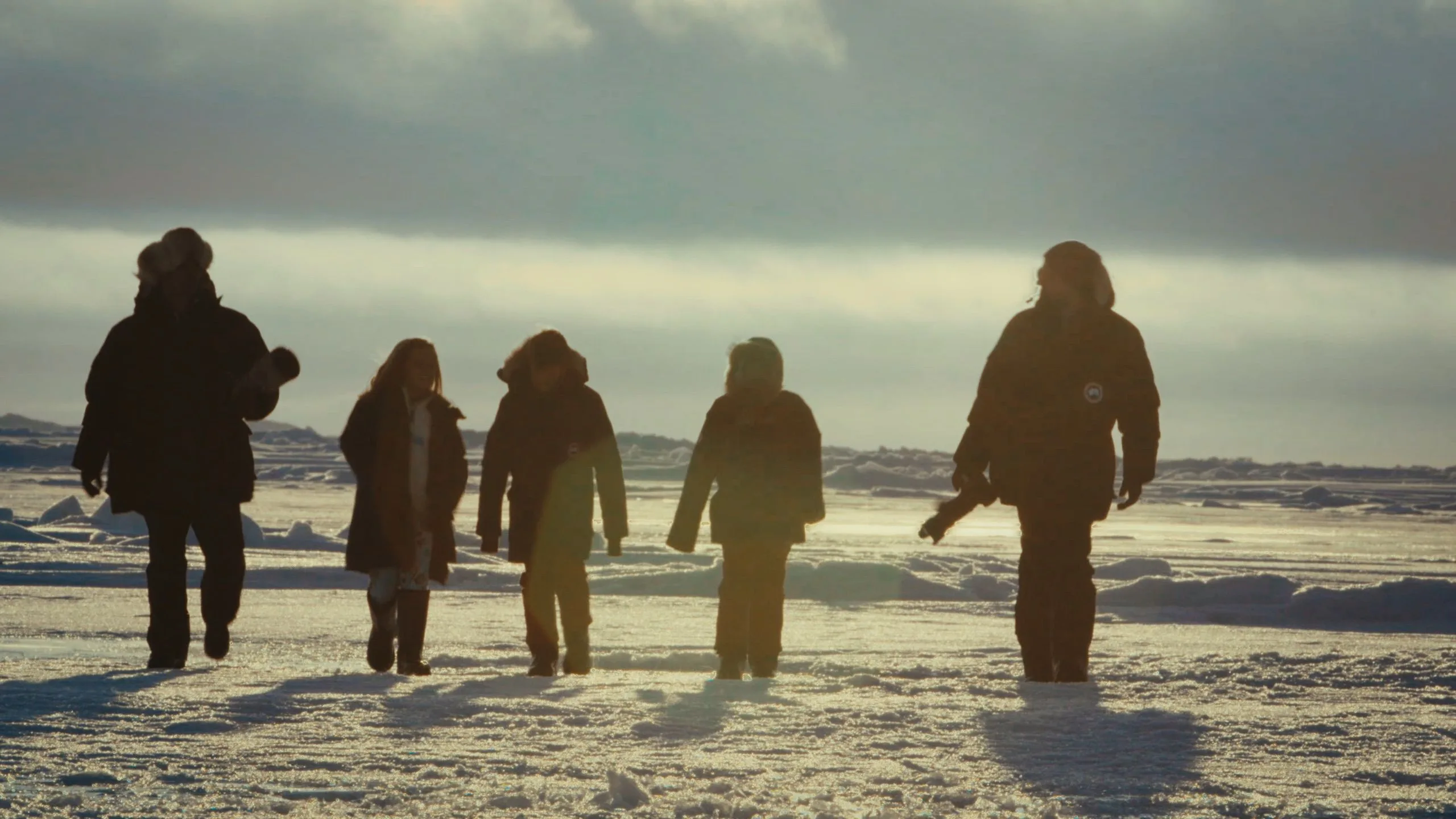 A group of five people walking in the snow. They are mostly silhouetted.