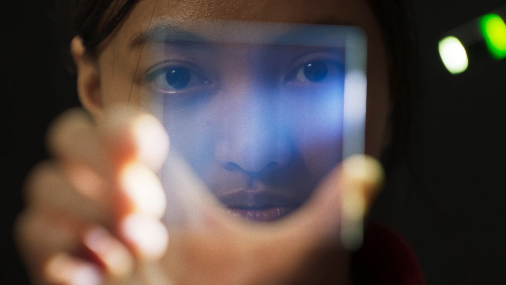 A girl is holding up a piece of glass with a light in it.