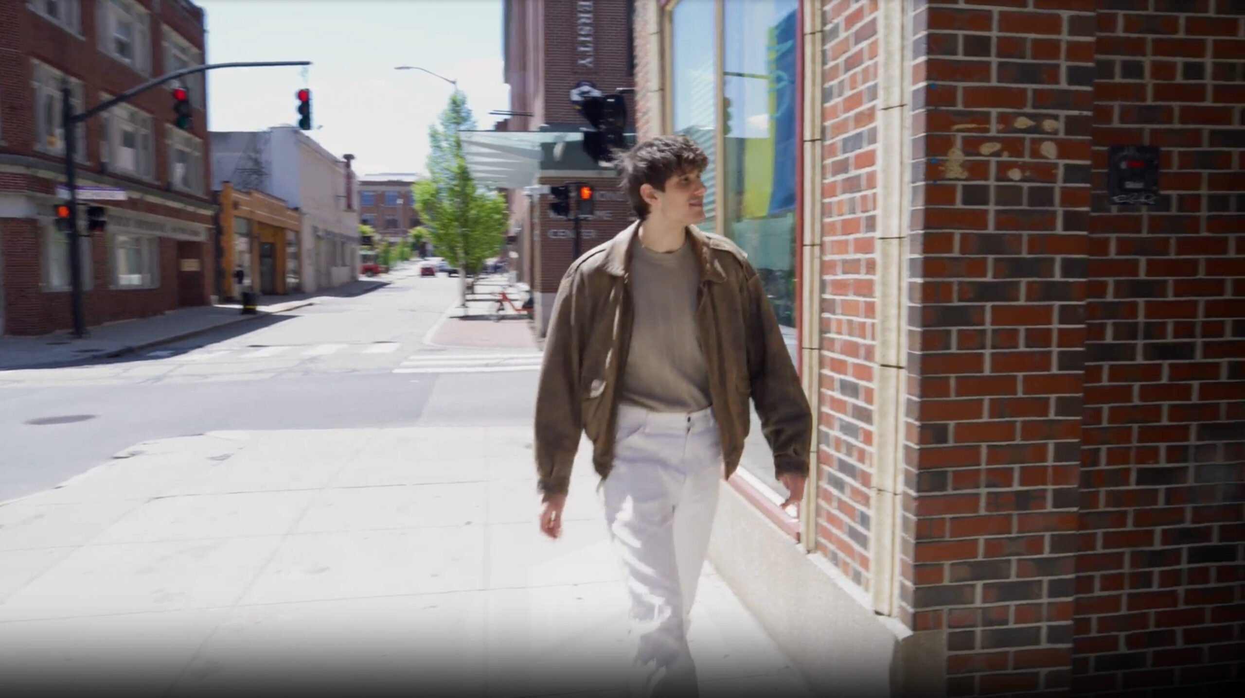 Man walking down city street in a brown jacket and white pants