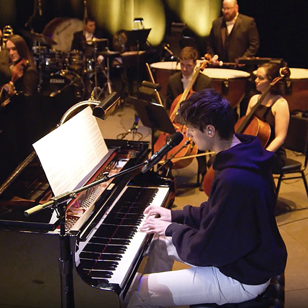 Man, pianist, and orchestra performing on stage