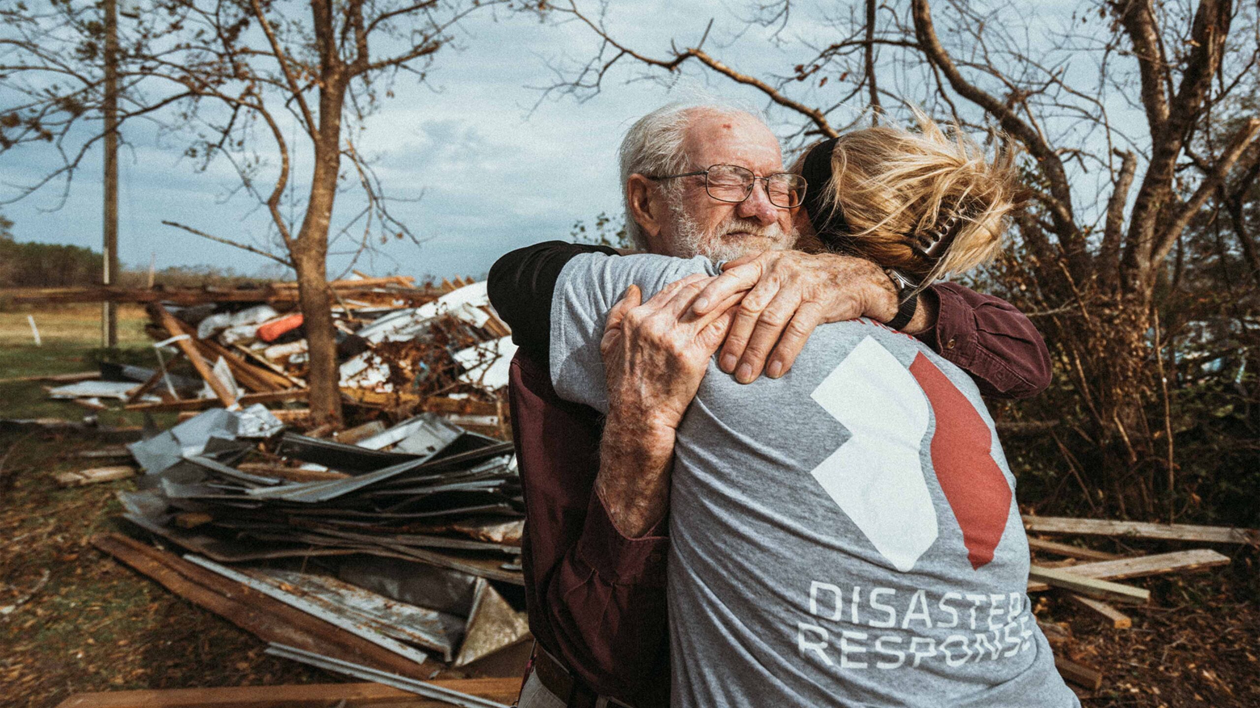 A man is hugging an older man in front of a pile of debris.