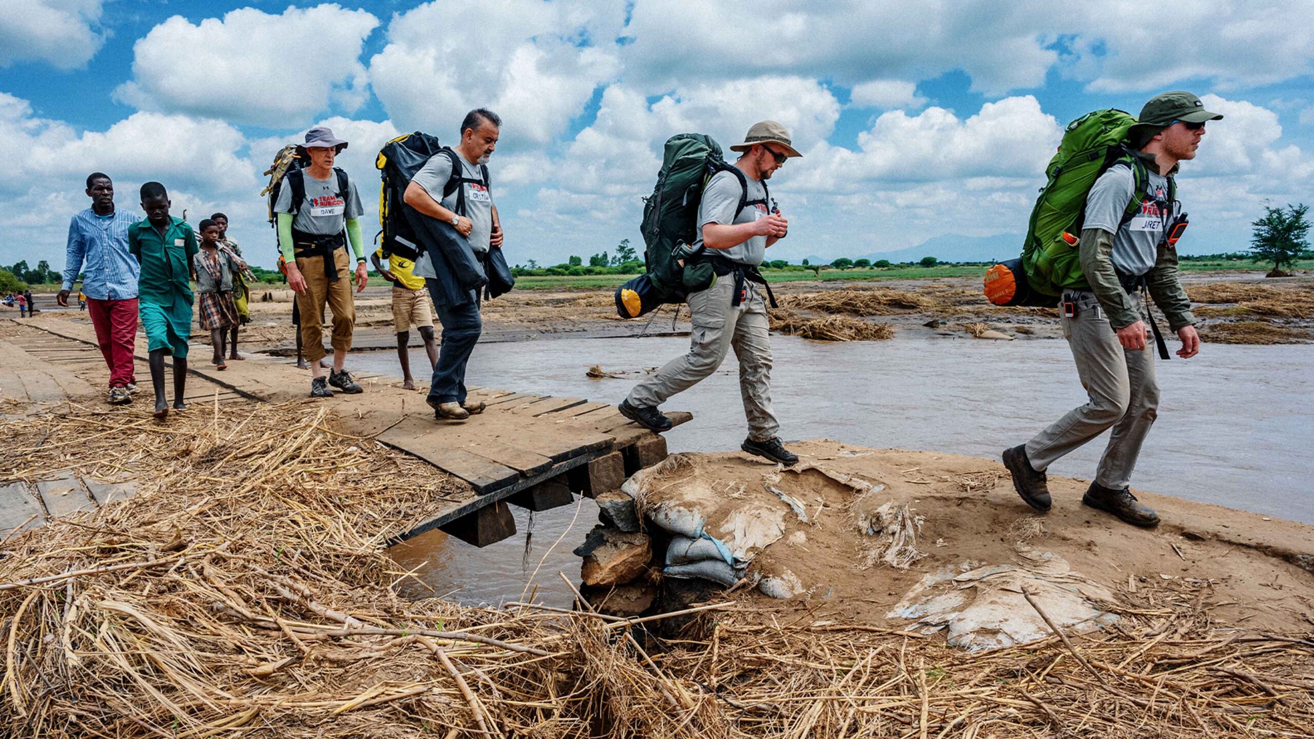 A group of people crossing a river with backpacks.