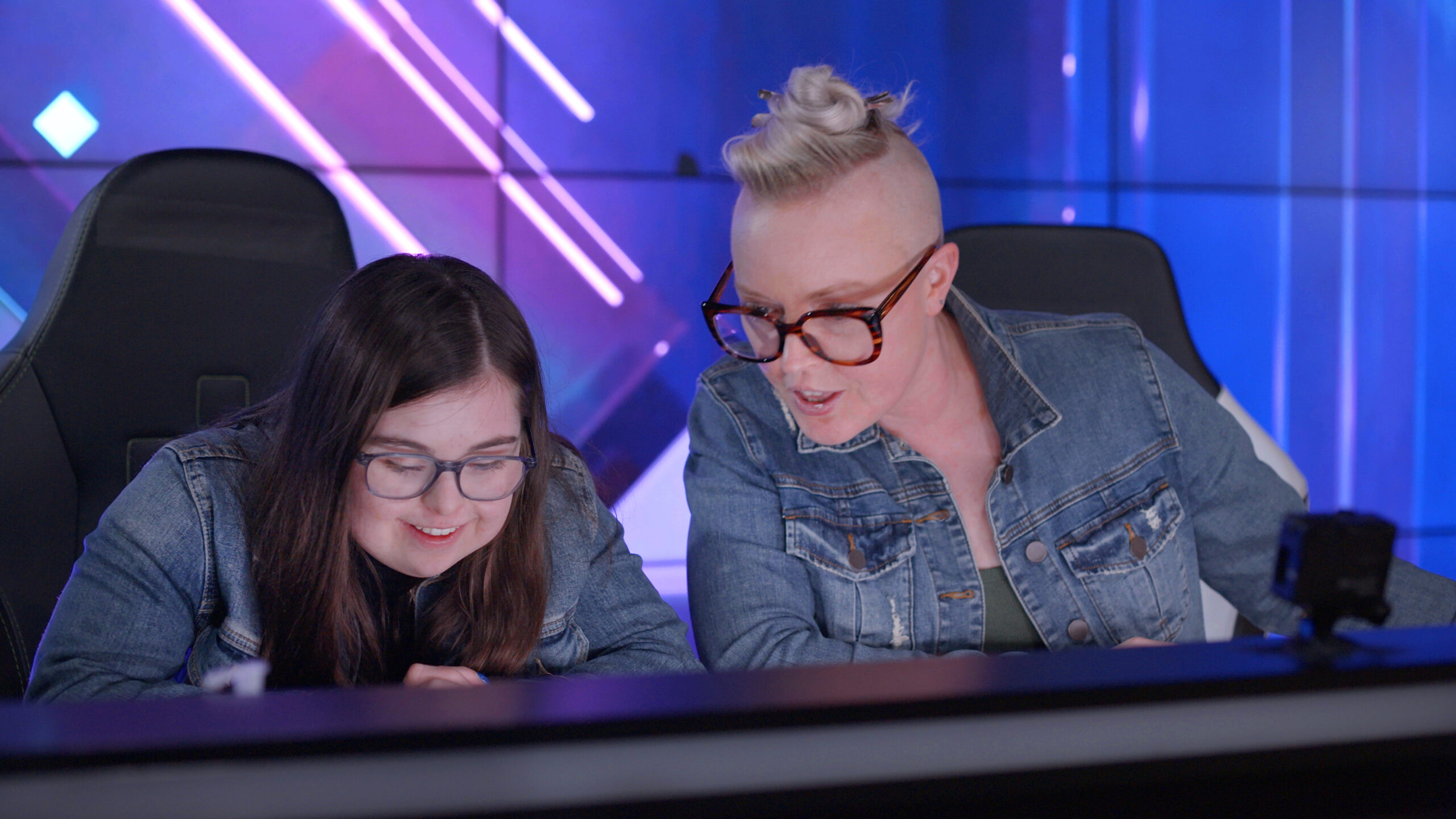 Two women seated looking toward desk in front of them.