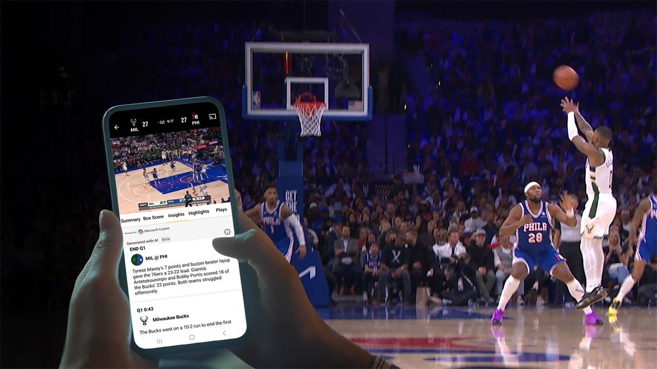 Person watching a basketball game on TV and following game updates on a smartphone in an arena.