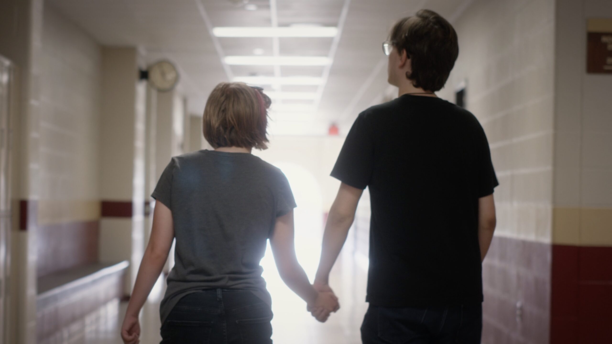 Two people holding hands walking down a hallway.