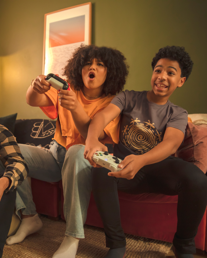 Two young adults excitedly playing video games on a couch, holding controllers and reacting animatedly.