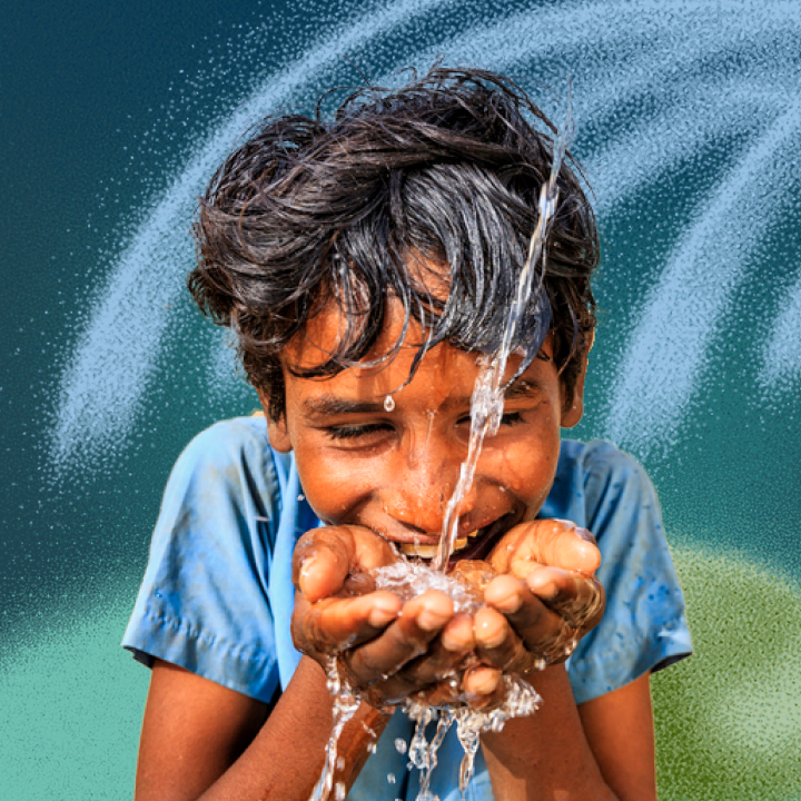 A boy in a blue shirt happily catches splashing water in his hands against a green background.