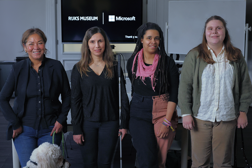 Four women of diverse backgrounds standing in a room with "rijksmuseum" and "microsoft" logos on screens in the background.