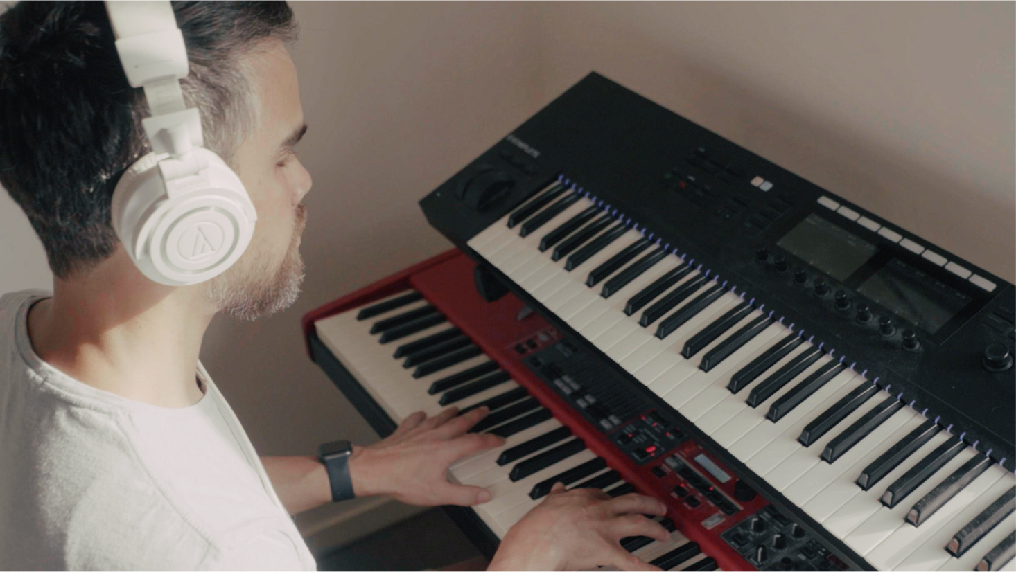 Man with headphones playing an electronic keyboard in a softly lit room.