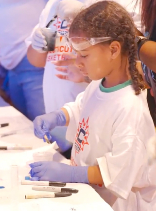 A young girl in safety goggles and gloves conducting a science experiment with test tubes and a pipette.