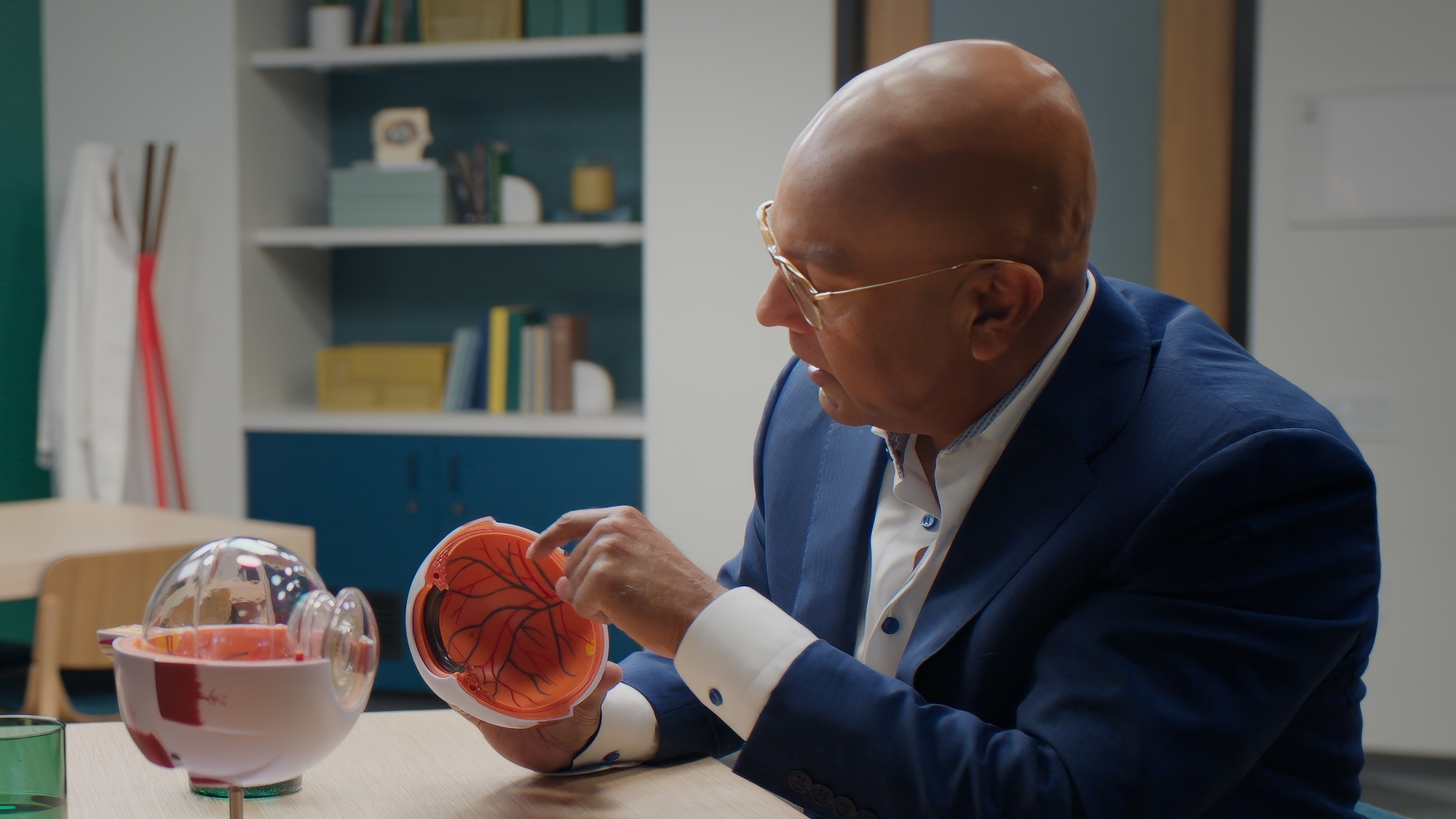 A man in a suit demonstrates a brain model at a table in an office setting.