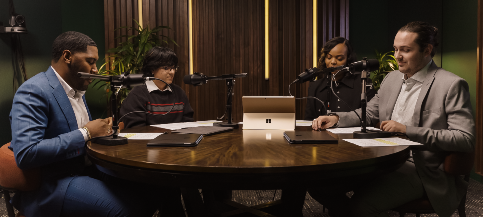 Four people are sitting around a round table with microphones, recording a podcast in a studio.