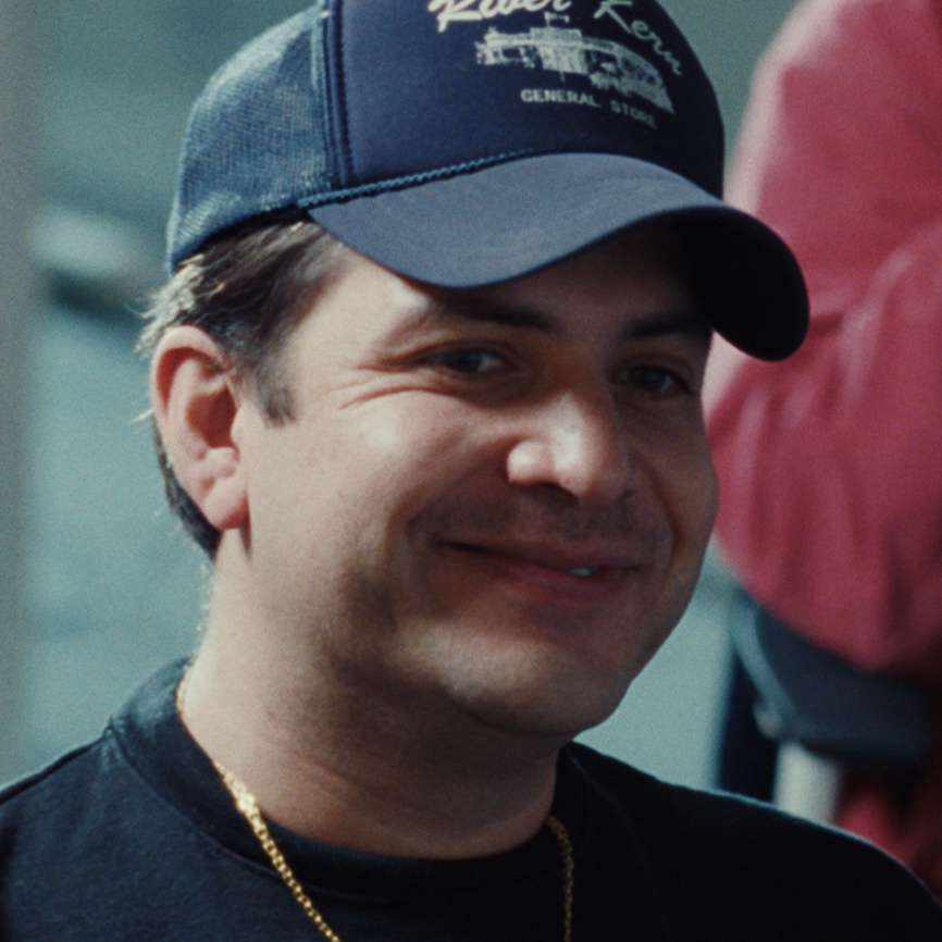 A person wearing a dark baseball cap and black shirt, smiling slightly.