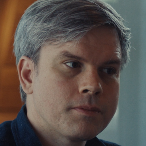 Man with short gray hair looking to the side, wearing a dark shirt.