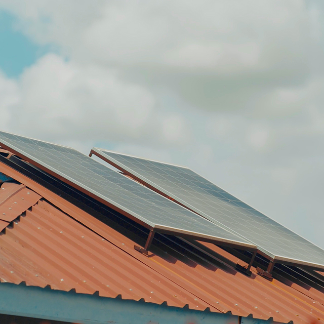 Solar panels installed on a slanted, red corrugated metal roof under a partly cloudy sky.