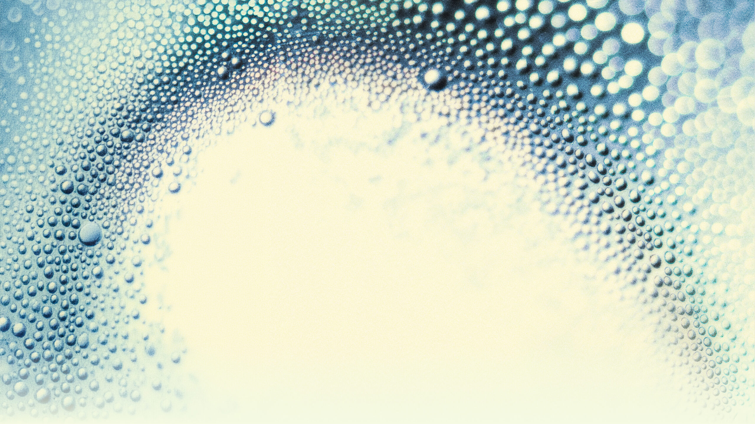 Abstract macro photograph of countless spherical droplets or bubbles arranged in flowing wave-like patterns, rendered in shades of blue, teal, and white with a depth-of-field blur effect.